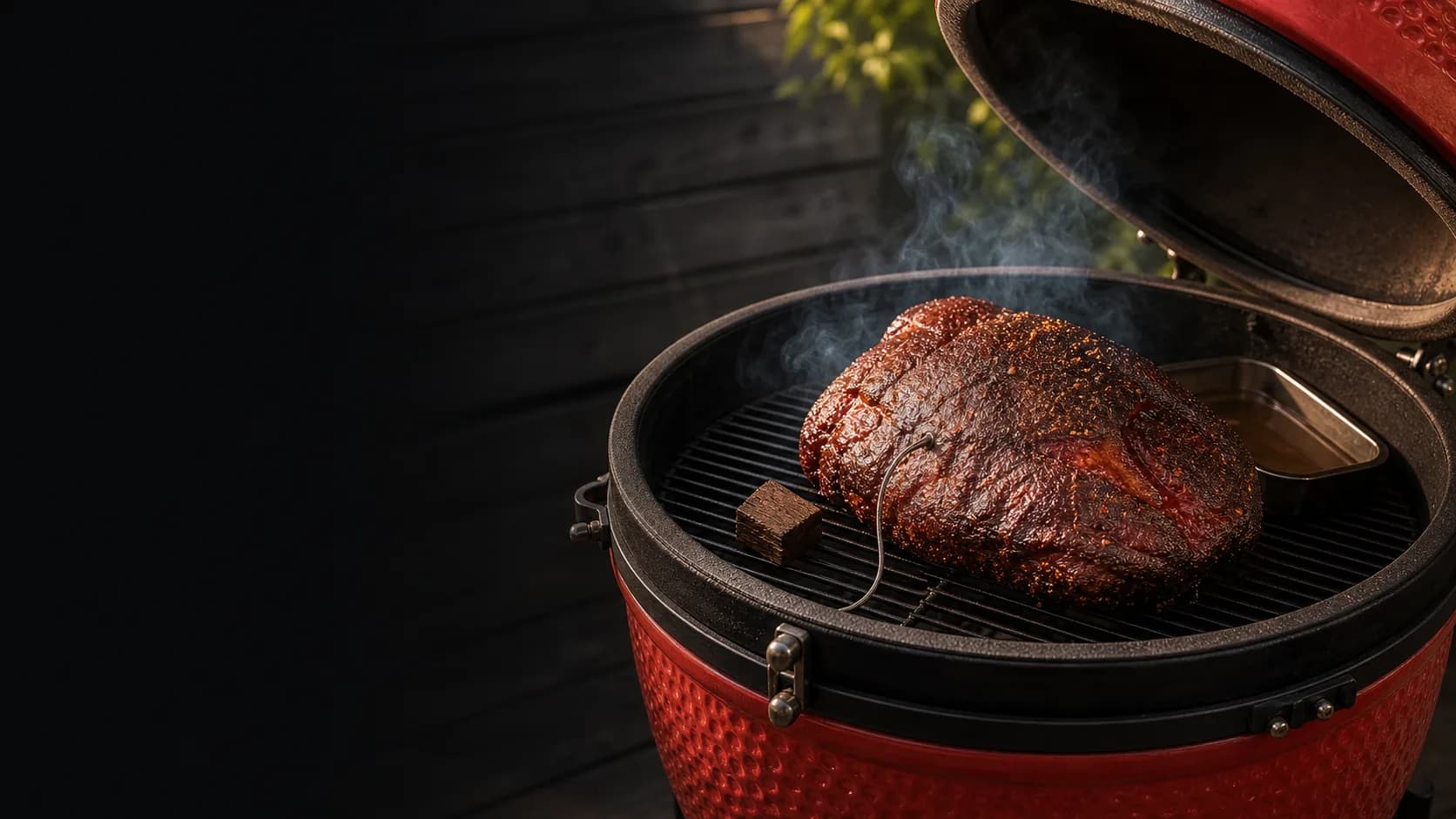 Low and slow BBQ en una kamado roja con humo, bark y termómetro